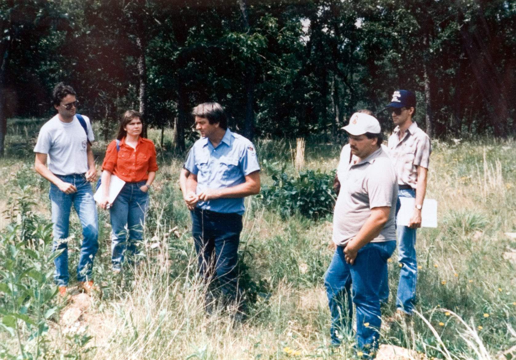 Three students standing in a field of grass as they listen to an instructor.