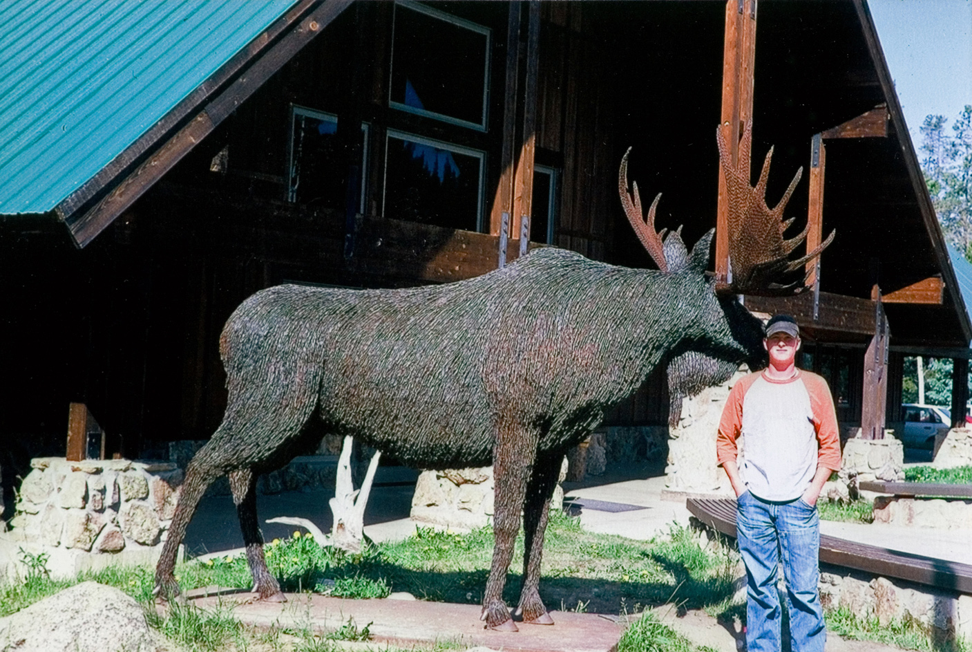 A student standing next to a large moose statue that is outside.