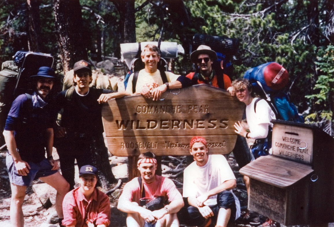 Students in hiking gear pose for a photo at the Comanche Peak trail sign.
