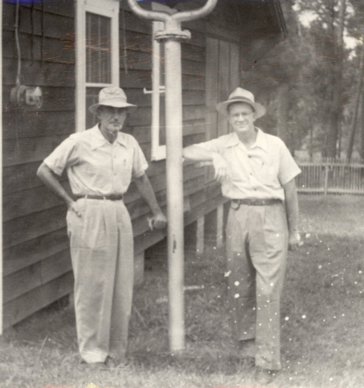 Two men are standing next to a pole posing for a photo.