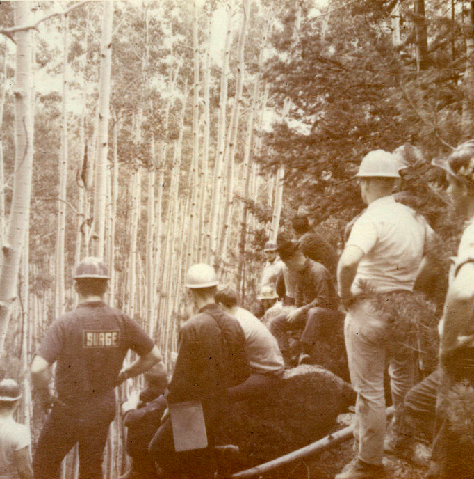 A group of students wearing hardhats outside in a forest. A group of students wearing hardhats outside in a forest.