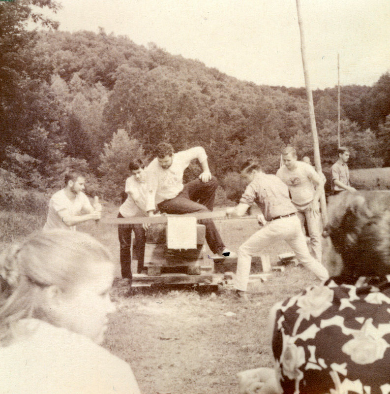 A group of people using a saw to cut a tree trunk. A group of people using a saw to cut a tree trunk.