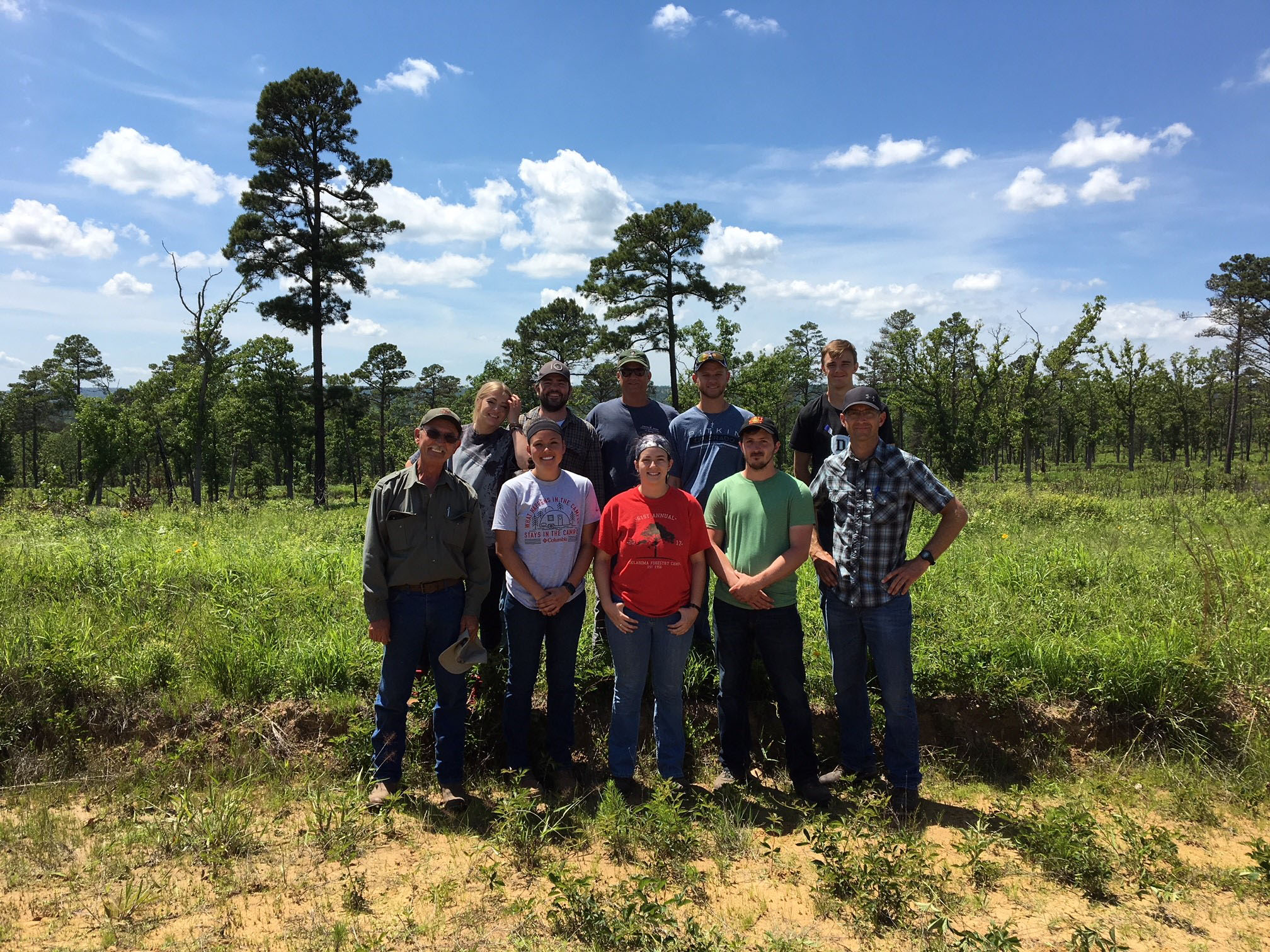 A group of ten individuals standing at the edge of a forest. 