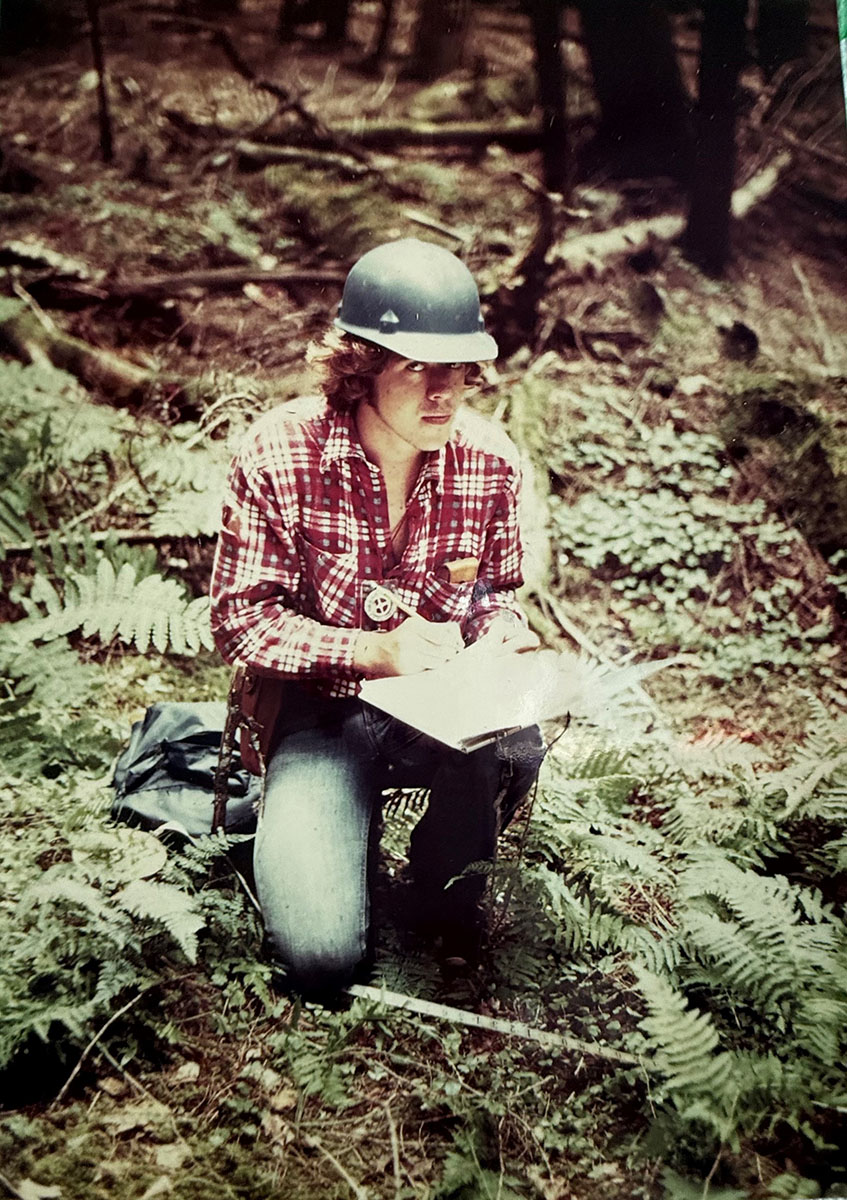 A person kneeling with a clipboard taking notes in the forest. A person kneeling with a clipboard taking notes in the forest.