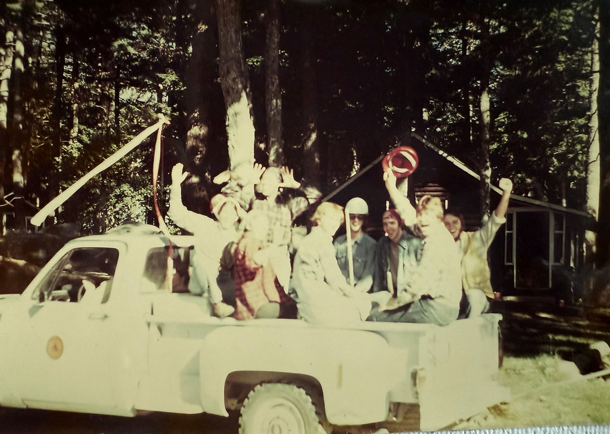 A group of people sitting and waving in the back of a pickup truck. A group of people sitting and waving in the back of a pickup truck.