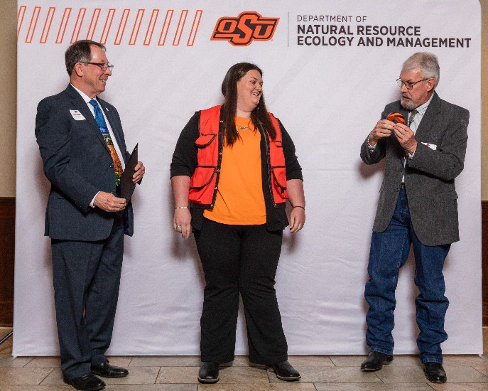 Savanah has on a orange vest next to Tom and Jim.