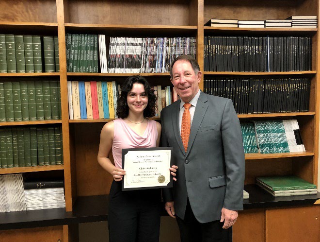 Claire Anderson is accepting her award from Jim Ansley in front of a book shelf. Claire Anderson is accepting her award from Jim Ansley in front of a book shelf.
