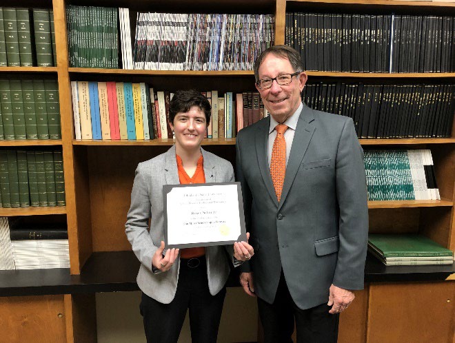 Renee Schuette is accepting her award from Jim Ansley in front of a book shelf. Renee Schuette is accepting her award from Jim Ansley in front of a book shelf.