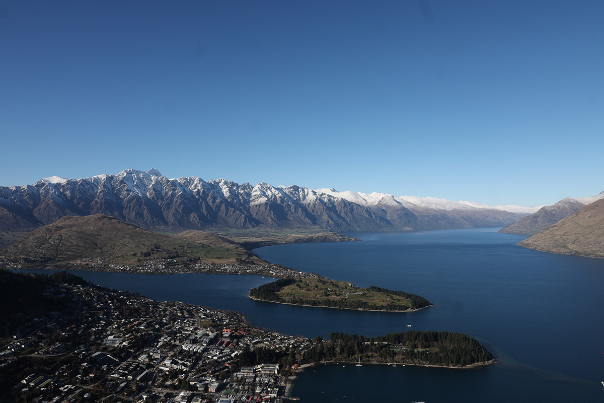 An aerial view of snow-capped mountains behind a body of water in New Zealand.