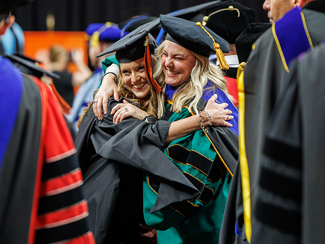 Student at graduation ceremony hugs a faculty member.